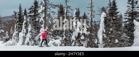 Snowshoeing woman hiking in snow in forest mountain. Winter sport activity on cold outdoor snowshoe trail hiker walking alone on landscape banner Stock Photo