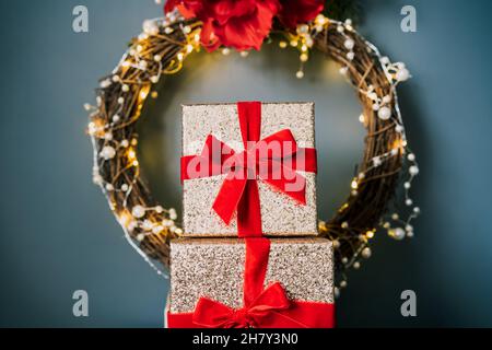 Close up tower of glittering golden gift boxes with velvet red ribbon on the elegant Christmas wreath background. Posh, luxury gifts packing. Festive Stock Photo