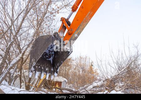 Excavator bucket over bushes and broken trees sticking out of the snow Stock Photo