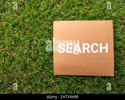 Brown card written with text SEARCH on a green grass background. Stock Photo
