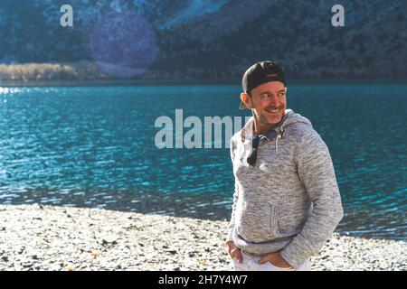 Man standing in front of mountain lake with ball cap on looking away  Stock Photo