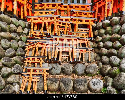 Small torii gates are stacked together on a rock wall at the Fushimi-Inari Shinto Shrine. Stock Photo