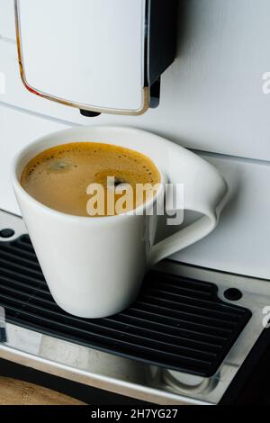 White cup of espresso with thick foam in coffee machine on table, top view from above Stock Photo