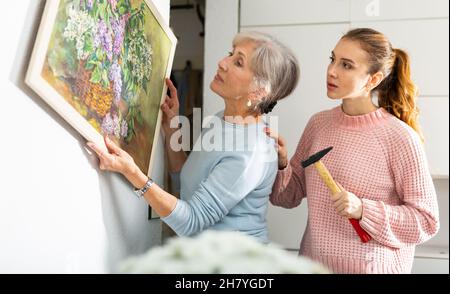 Young woman helping elderly mother to hang painting on wall Stock Photo