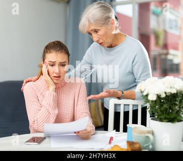 Worried elderly woman with adult daughter checking utility bills Stock Photo