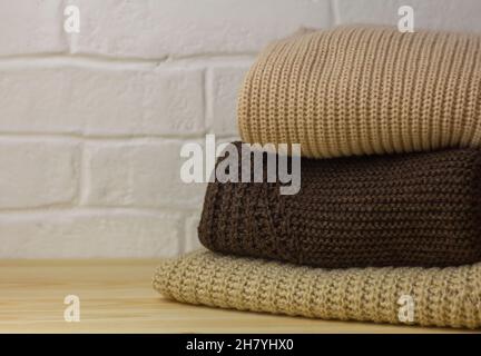 A pile of warm sweaters and jumpers on a wooden table on a light background.Warm autumn and winter clothes Stock Photo