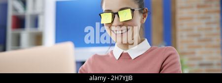 Young smiling woman with yellow stickars on glasses with question mark works on laptop Stock Photo