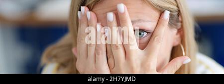 Woman covers face with her hand looking through fingers closeup Stock Photo