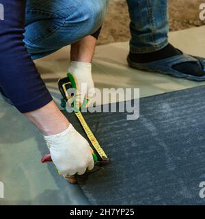 The master prepares bitumen tape for installation, protection of a floor from moisture, measurement and cutting. Stock Photo