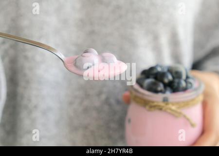 Female hands holding Bowl with yogurt and blueberries on table. Woman eating Blueberry yogurt with fresh blueberries. Healthy breakfast. Super food Stock Photo