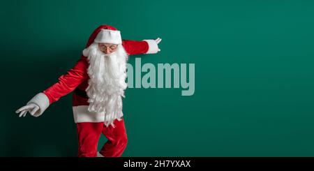 Emotional actor in costume of Santa Claus with long beard gestures and poses on green background Stock Photo