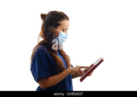 Female doctor in a face mask and surgical uniform using a digital tablet while standing on an isolated background. Stock Photo