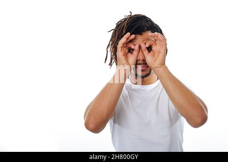 Man holds hands near eyes and pretends to look through binoculars while standing on an isolated background. Stock Photo