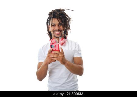 Latin man with headphones using a mobile phone while standing over an isolated background. Stock Photo