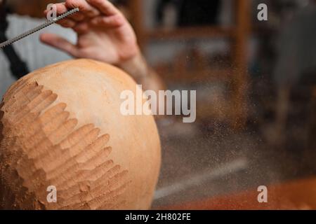 Anonymous male master in apron using rasp to shape round wooden piece while working in professional joinery with various sculptures Stock Photo