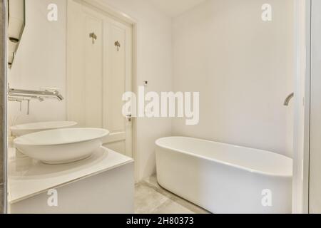 White ceramic washbasins with stainless taps placed at wall against bathtub in modern light bathroom with closed door in apartment Stock Photo