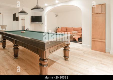 Interior of modern billiard room with pool table under chandeliers near relaxing area with sofa and tv on wall Stock Photo