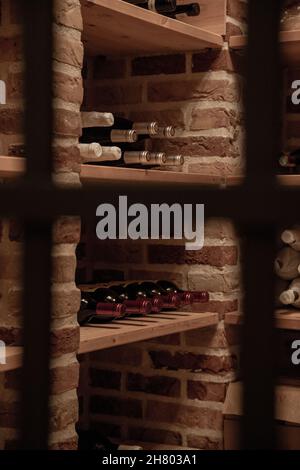 Bottles of various wine placed on wooden shelves in illuminated storage with brick walls Stock Photo