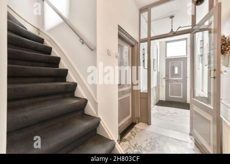 Stairway with gray steps and railing in corridor of contemporary house with closed door and decorative elements with marble floor Stock Photo