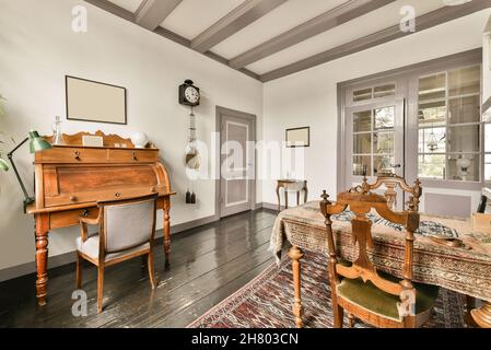 Vintage wooden secretary desk with chair placed in room near table with old fashioned tablecloth and door in retro styled apartment Stock Photo
