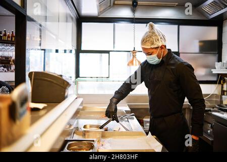 Close-up of professional latin chef man wearing a protective mask and uniform while working at restaurant kitchen. Stock Photo