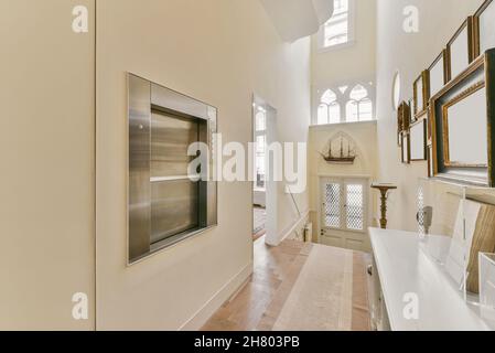 Corridor with collection of empty photo frames hanging on white wall near shelf with decorations in light apartment with doorway Stock Photo