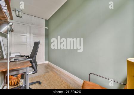 Armchair at wooden table with modern computer placed in small light room with floor lamp and green wall in apartment Stock Photo
