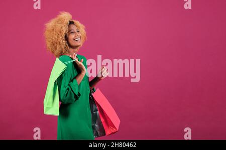 Young afro woman holds shopping bags on an isolated background. Black Friday sale concept. Stock Photo