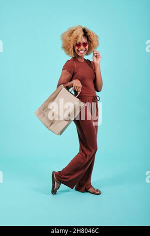 Portrait of a smiling African American woman holding shopping paper bags on an isolated light blue background. Stock Photo