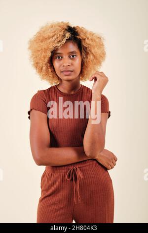 Curly haired woman looking seriously to the camera while standing on an isolated background. Stock Photo