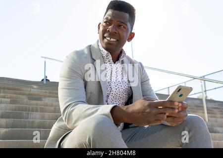 African American male in formal wear sitting on staircase and using cellphone Stock Photo