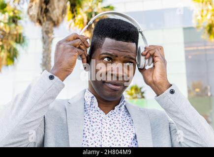 Black male entrepreneur in formal wear listening to music in wireless headphones looking away Stock Photo
