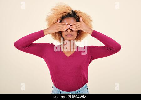 Serious afro woman covering eyes with hands while standing on isolated background. Stock Photo