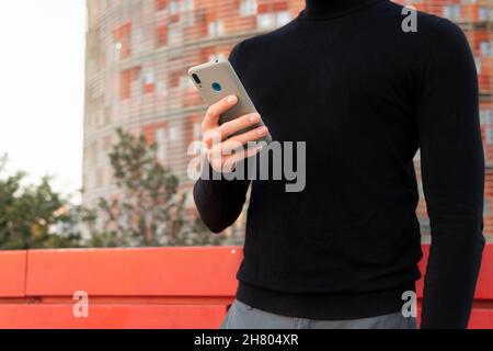 Handsome Asian male text messaging on cellphone on street near modern building in city Stock Photo