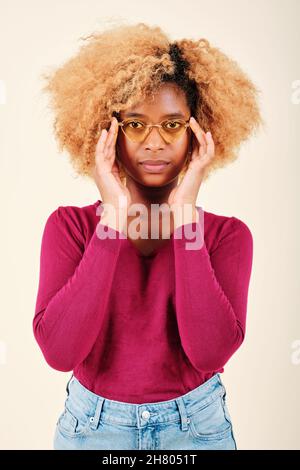 Woman with afro hairstyle wearing sunglasses while looking seriously at the camera. Stock Photo
