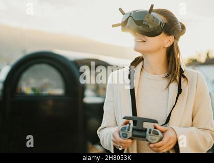 Positive anonymous female in modern black VR headset with remote controller standing on street of town while exploring virtual reality Stock Photo