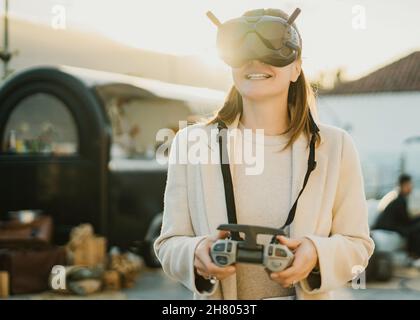 Positive anonymous female in modern black VR headset with remote controller standing on street of town while exploring virtual reality Stock Photo