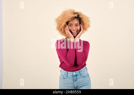 Happy afro woman looking surprised at the camera while posing against an isolated background. Stock Photo