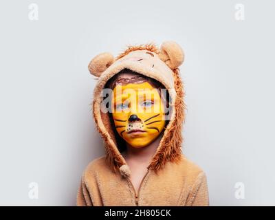 Sad boy in lion outfit with painted face wearing hood with mane looking at  camera on white background in studio Stock Photo - Alamy