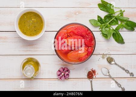Top view of peeled tomatoes placed on wooden table with olive oil and basil leaves near garlic and various spices for marinara sauce Stock Photo