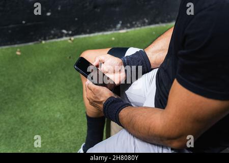 Cropped unrecognizable muscular sportsman in sportswear using cellphone while resting after intense workout in gym Stock Photo