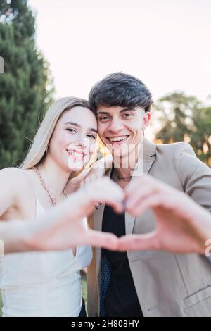 Delightful loving man and Woman smiling and looking at camera while making heart with hands in nature Stock Photo