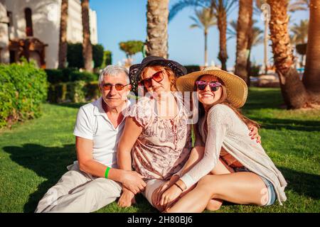 Senior couple relaxing on grass with adult daughter by hotel in Egypt. Happy people enjoying vacation on tropical resort in Sharm el Sheikh. Family va Stock Photo