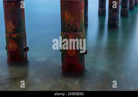 rusting and corroded metal piles on an old pier, abstract of sea and rusty pillars, mysterious and atmospheric moody image of corrosion on old jetty. Stock Photo