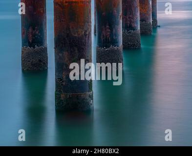 rusting and corroded metal piles on an old pier, abstract of sea and rusty pillars, mysterious and atmospheric moody image of corrosion on old jetty. Stock Photo