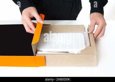 Man in black uniform unpacking a retail box with a new wifi router. Upgrading to the latest generation of the main networking device. Stock Photo