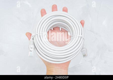 Roll of ethernet cable in hand against a grey background. Stock Photo