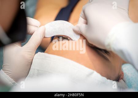 The beautician is gluing a patch under her eyes, before the procedure of eyelash extension. Artificial extended eyelashes Stock Photo