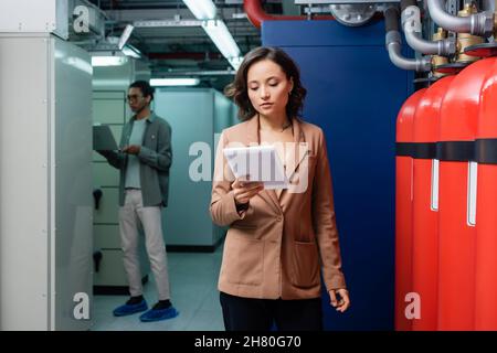engineer with digital tablet checking equipment in data center near blurred african american colleague Stock Photo