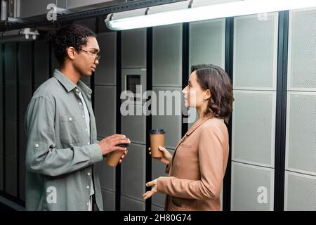 side view of multiethnic technicians with coffee to go talking in data center Stock Photo